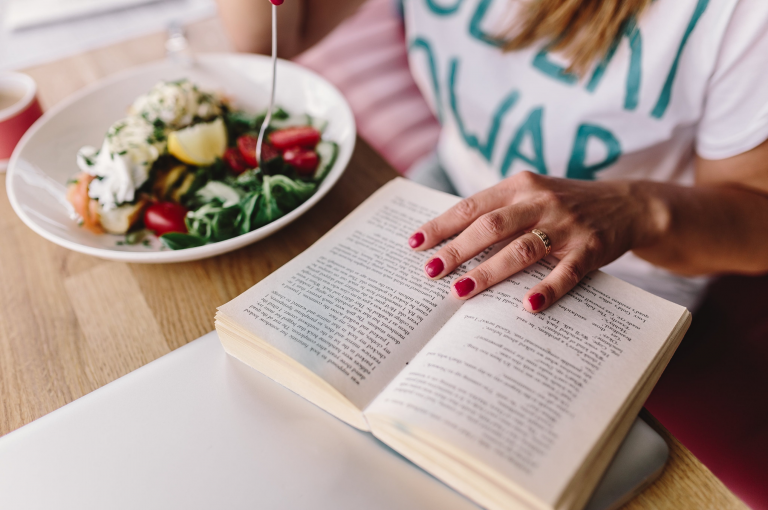 Donna che legge un libro con ciotola di insalata